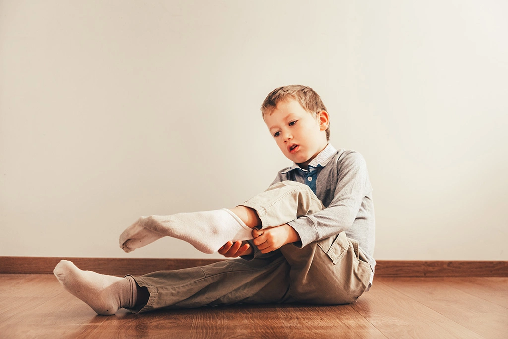 Child sitting on floor putting socks on