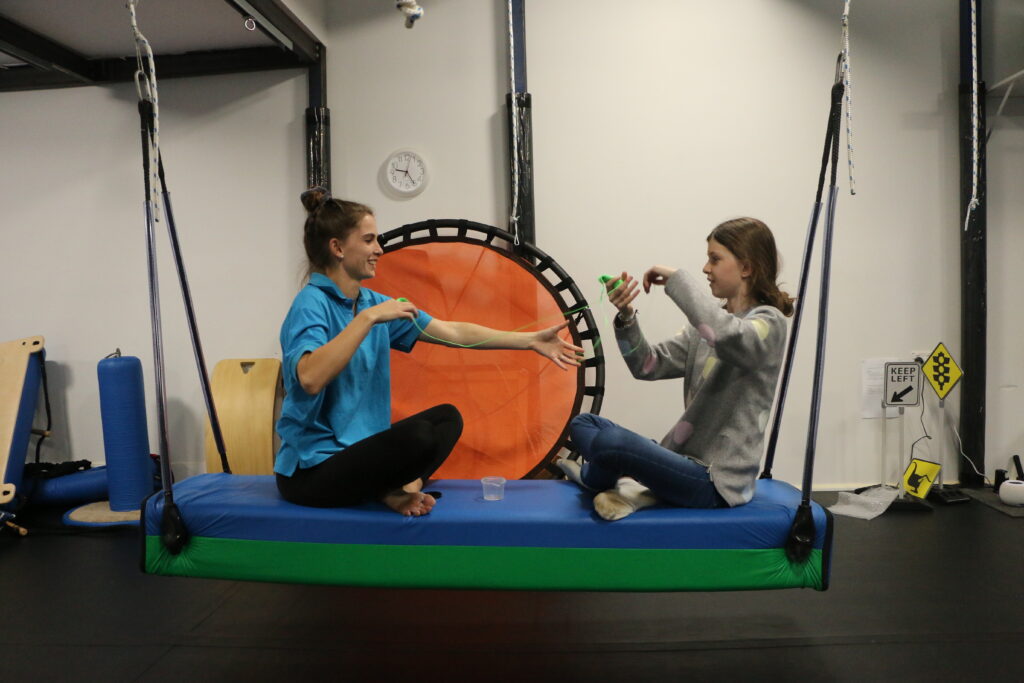 a therapist and child play with theraputty on a swing in an occupational therapy clinic