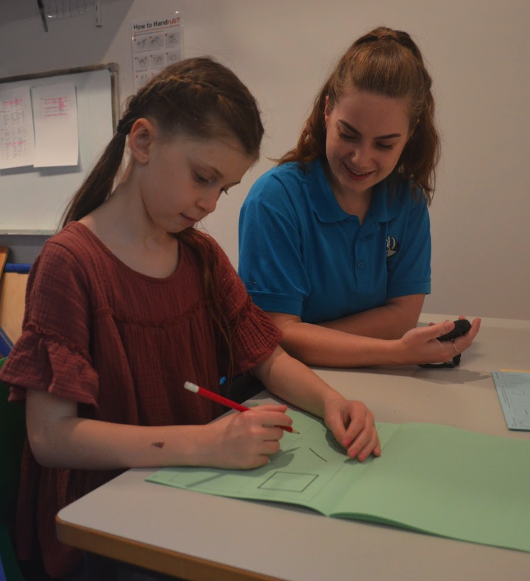 An occupational therapist completes an assessment with a young girl, sitting at a table in a clinic room